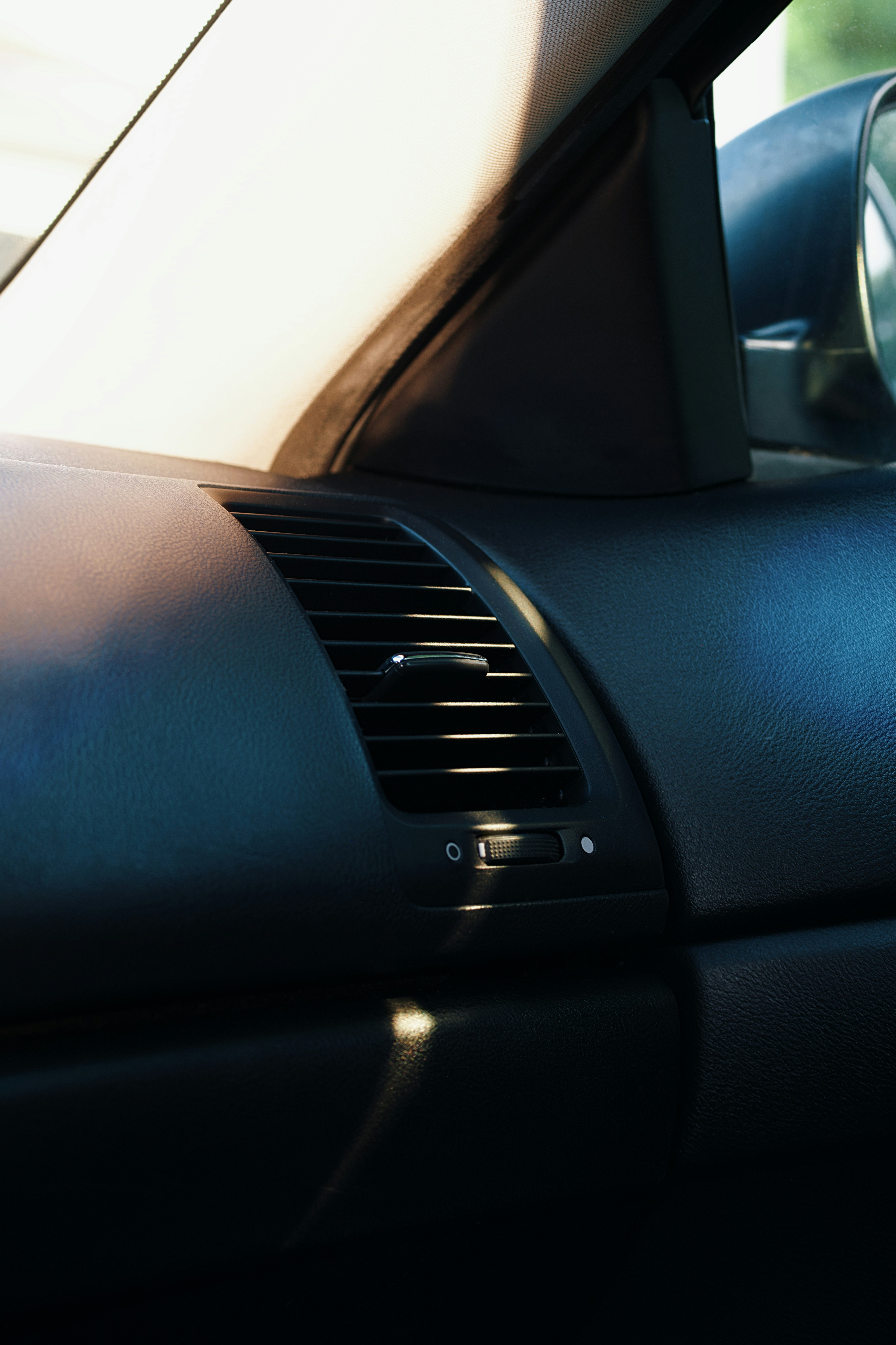 Car dashboard with air vent and sunlight.