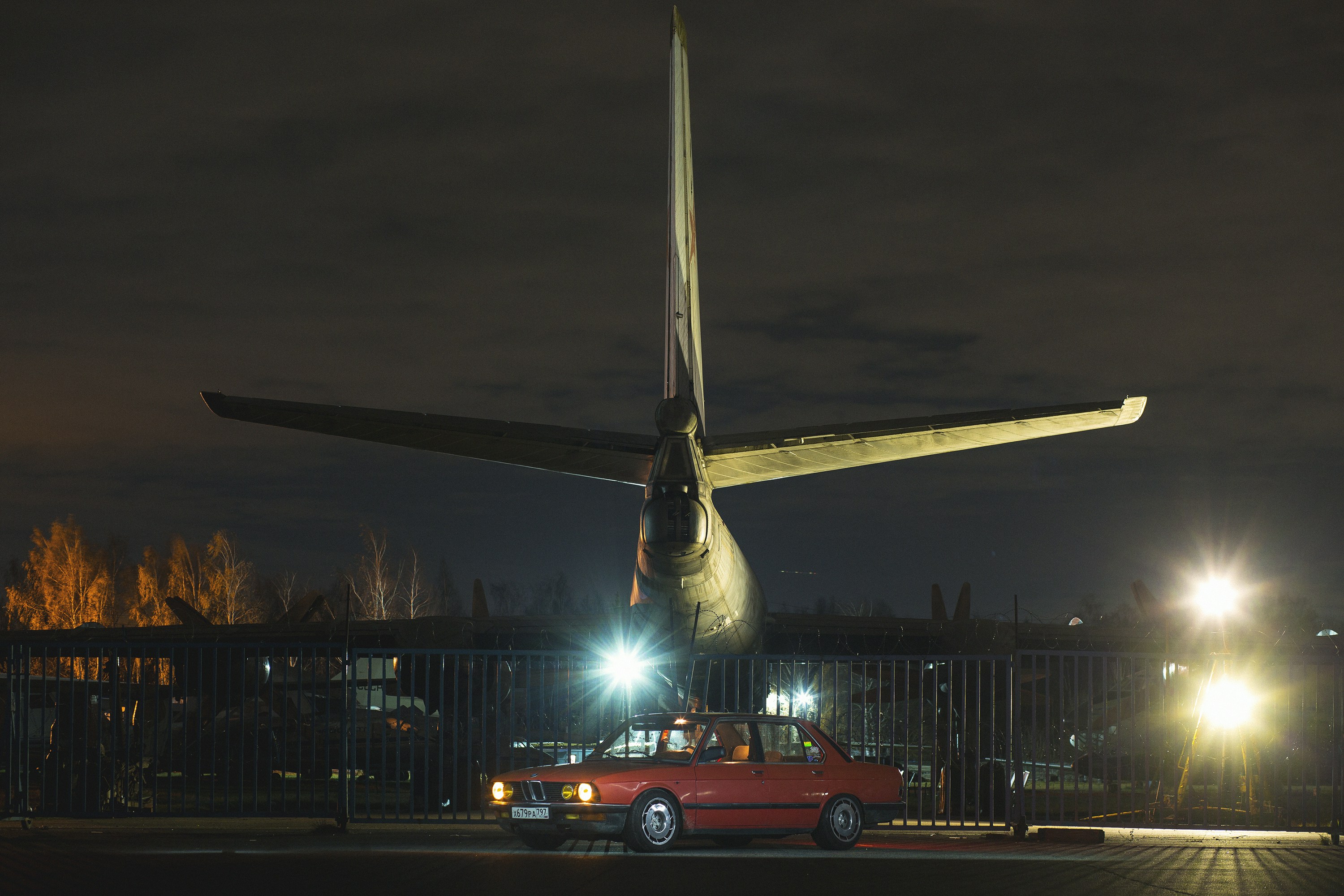 A car parks under an airplane's tail at night.