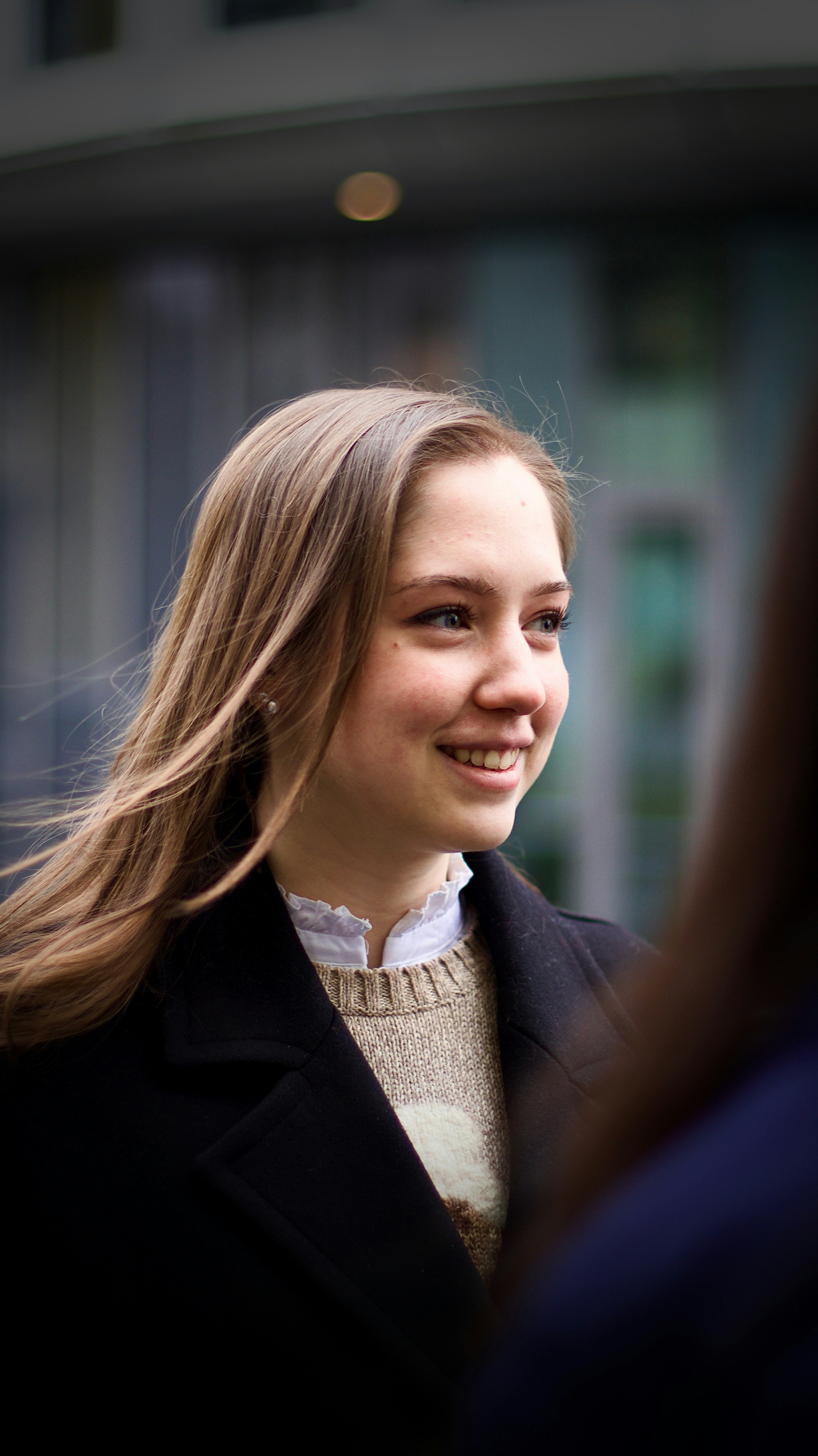 A young woman smiles outdoors, looking happily.