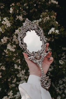 A hand holds a decorative antique mirror.