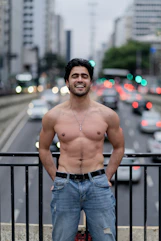 Man smiles shirtless in front of a busy road.