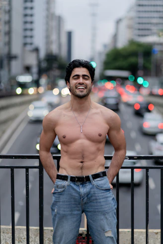 Man smiles shirtless in front of a busy road.