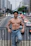 A shirtless man leans on a bridge, smiling.