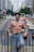 A shirtless man leans on a bridge, smiling.