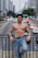 A shirtless man leans on a bridge, smiling.