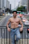 A shirtless man leans on a bridge, smiling.