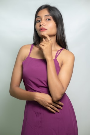 A woman ponders, wearing a purple dress.