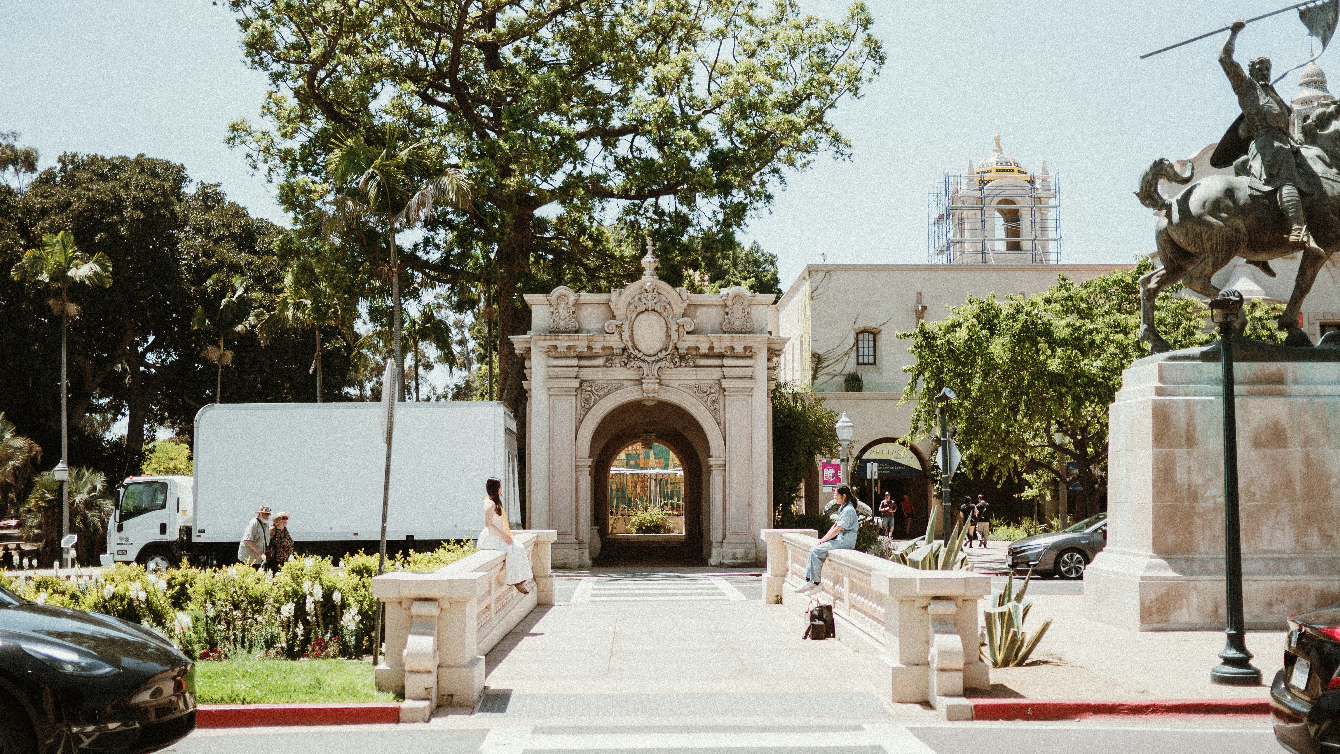 A park entrance with a statue and buildings.