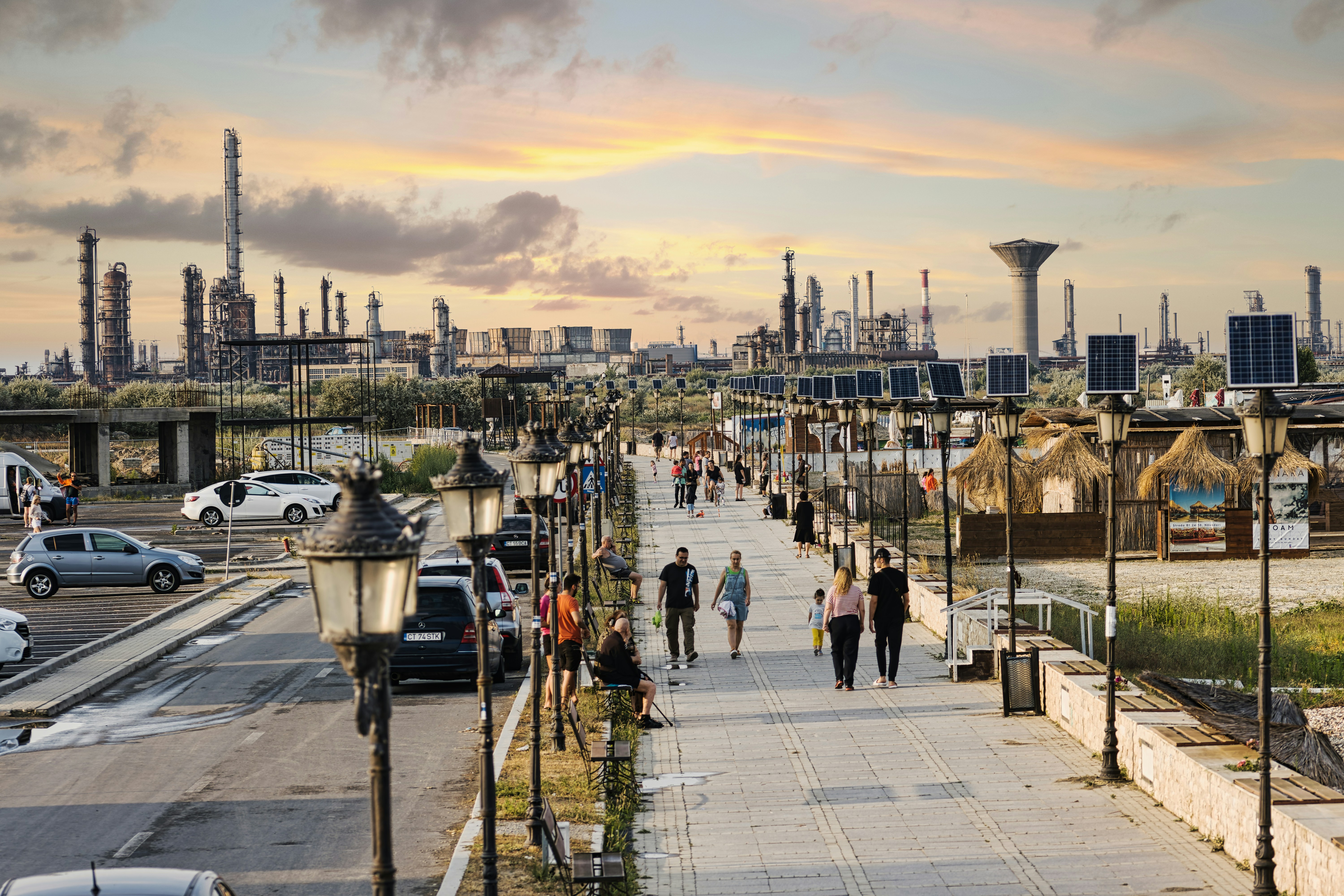 People walk on a path with an industrial backdrop.