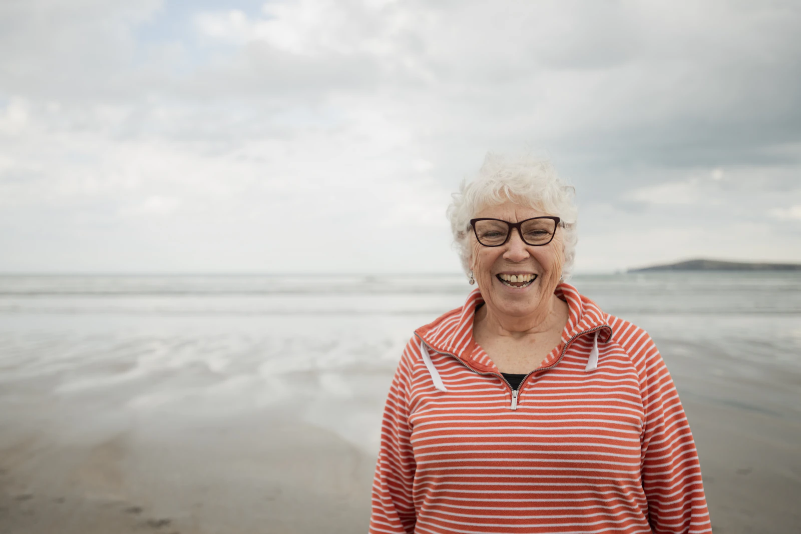 Femme âgée souriante aux cheveux blancs, portant un pull rayé, en extérieur