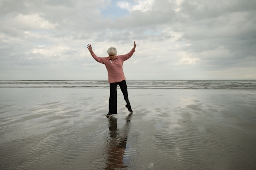 Woman stands at the beach with arms raised.