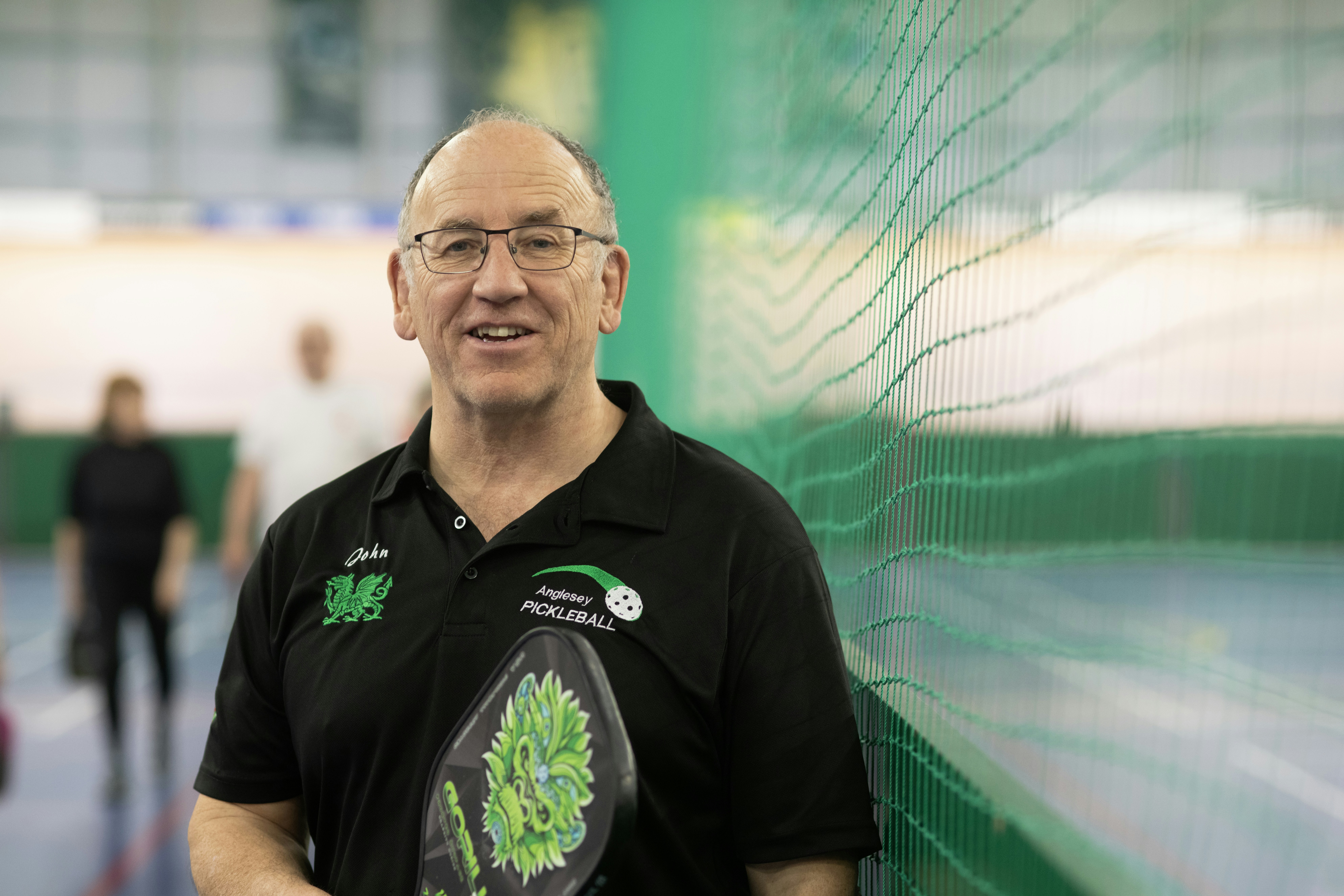 A smiling man holds a pickleball paddle.