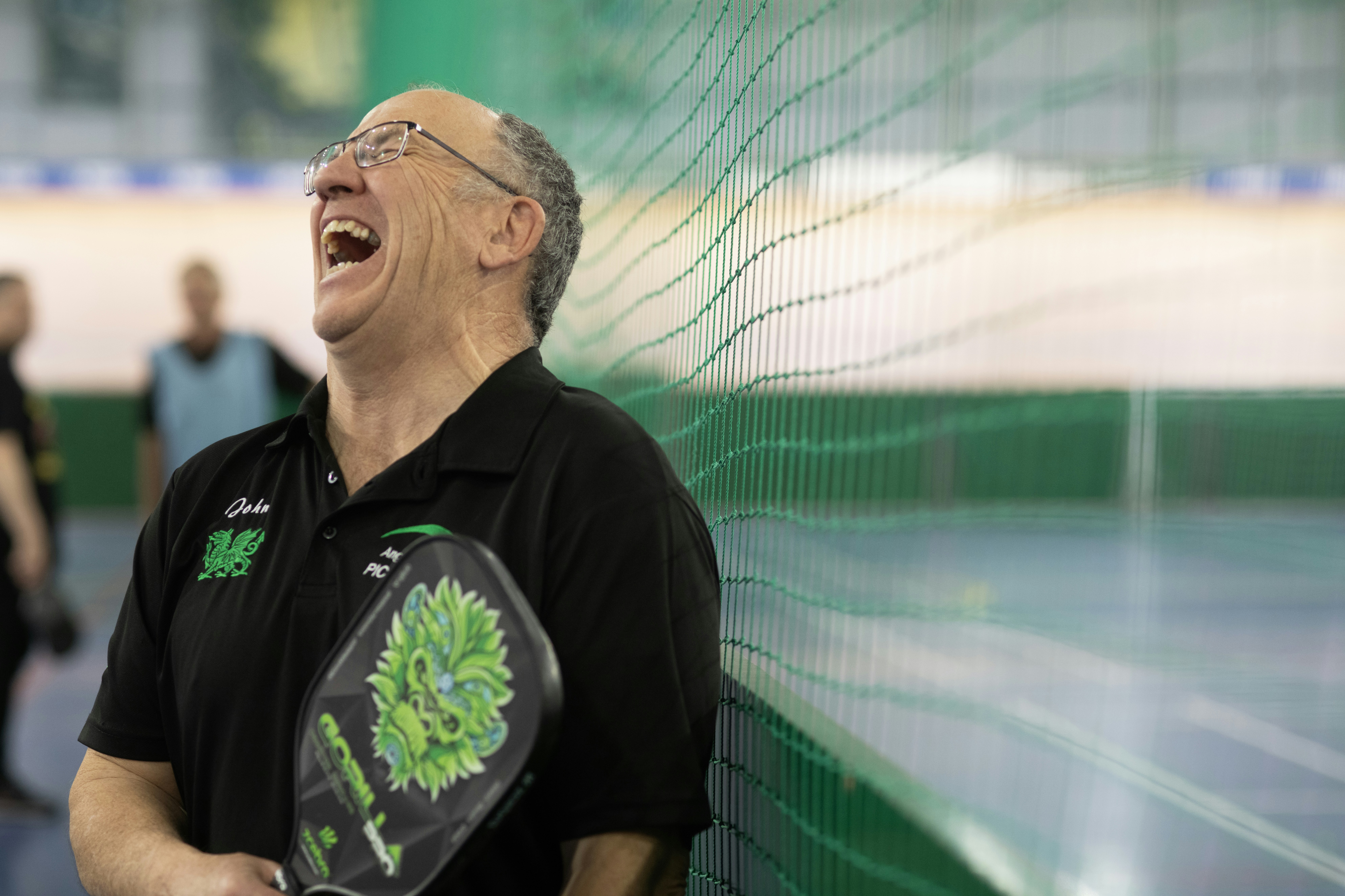 The man is laughing with a pickleball paddle.