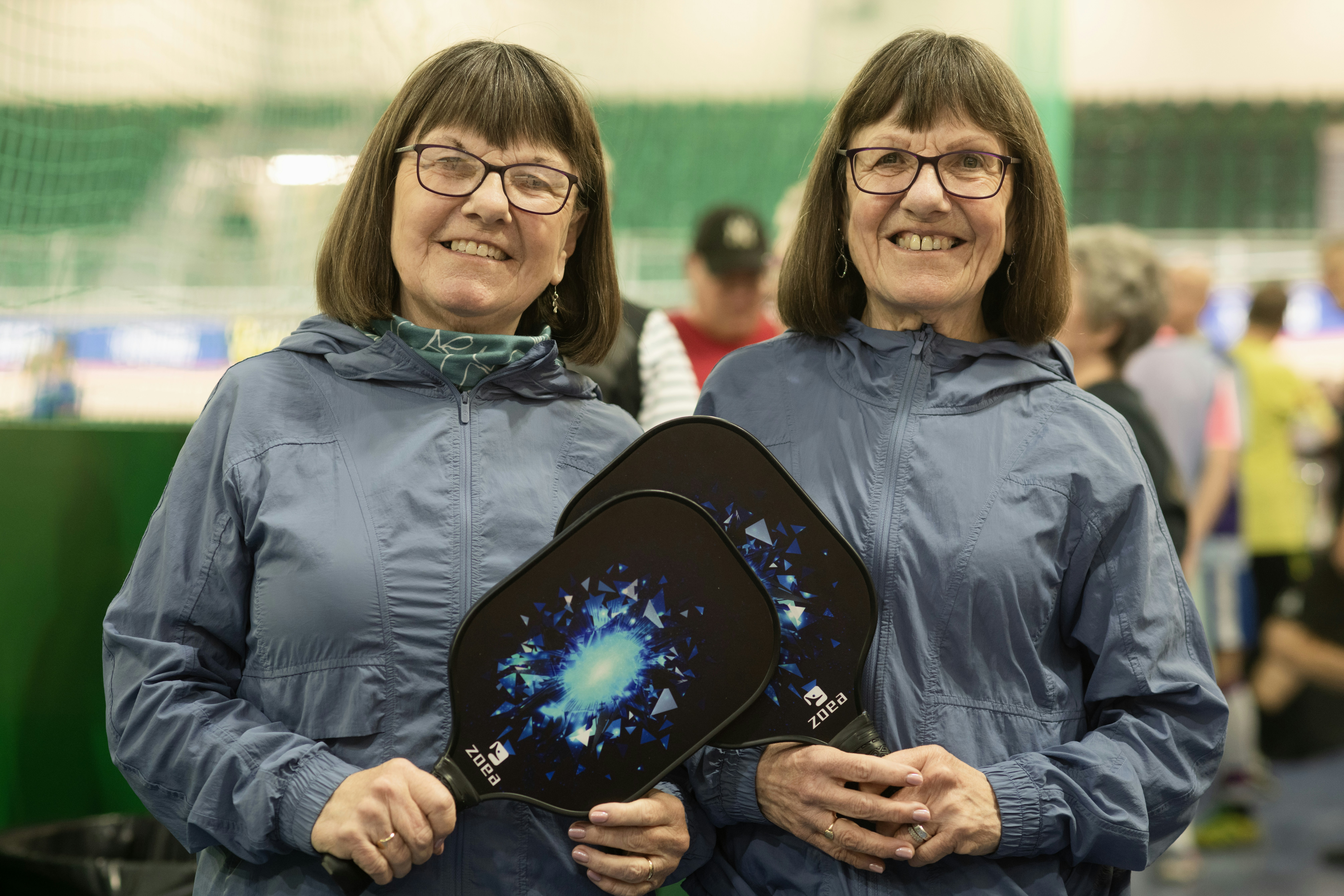Two women smile holding pickleball paddles.