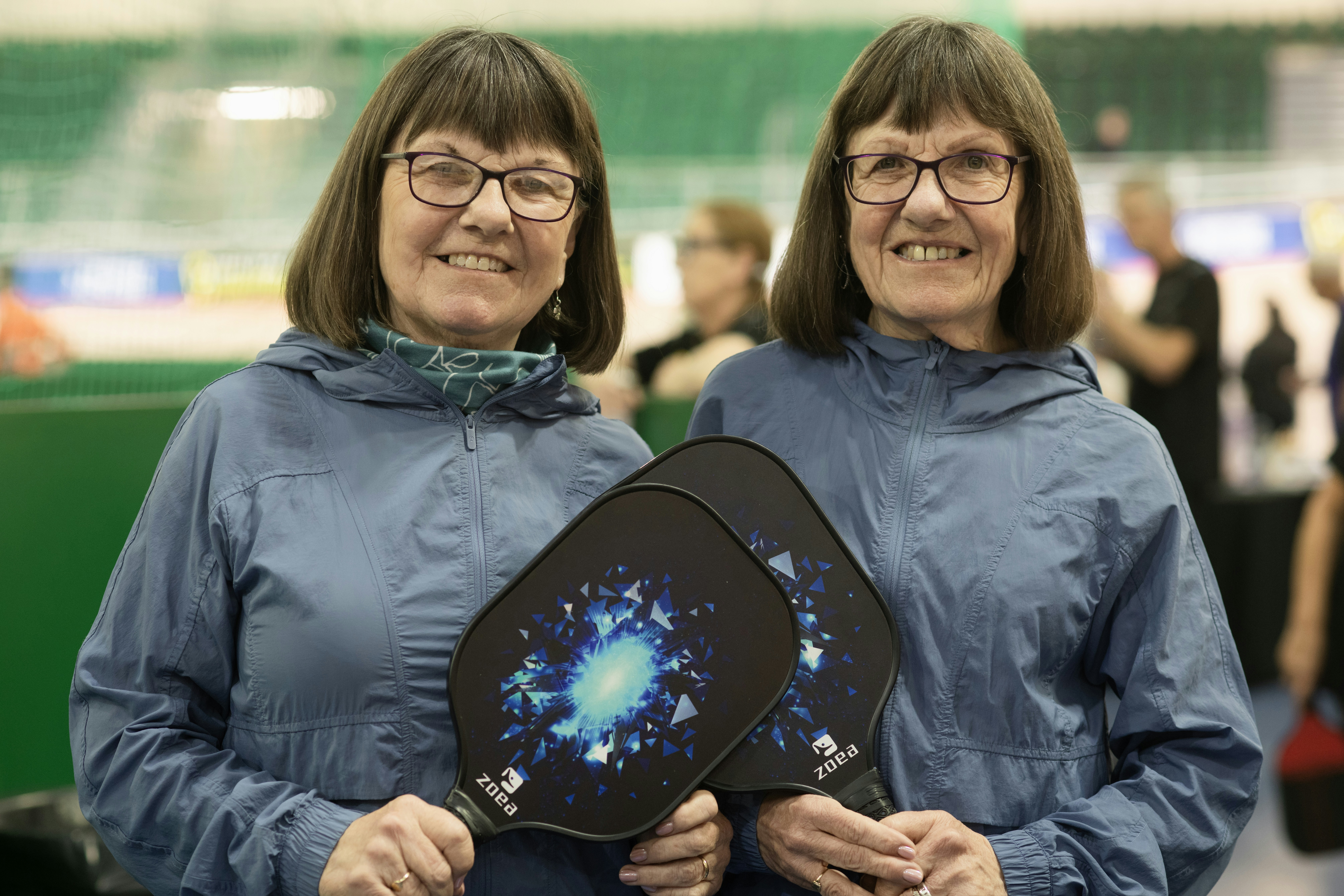 Two smiling women hold pickleball paddles.