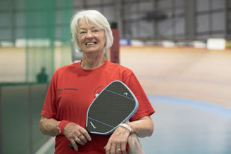 Smiling woman holding a pickleball paddle.