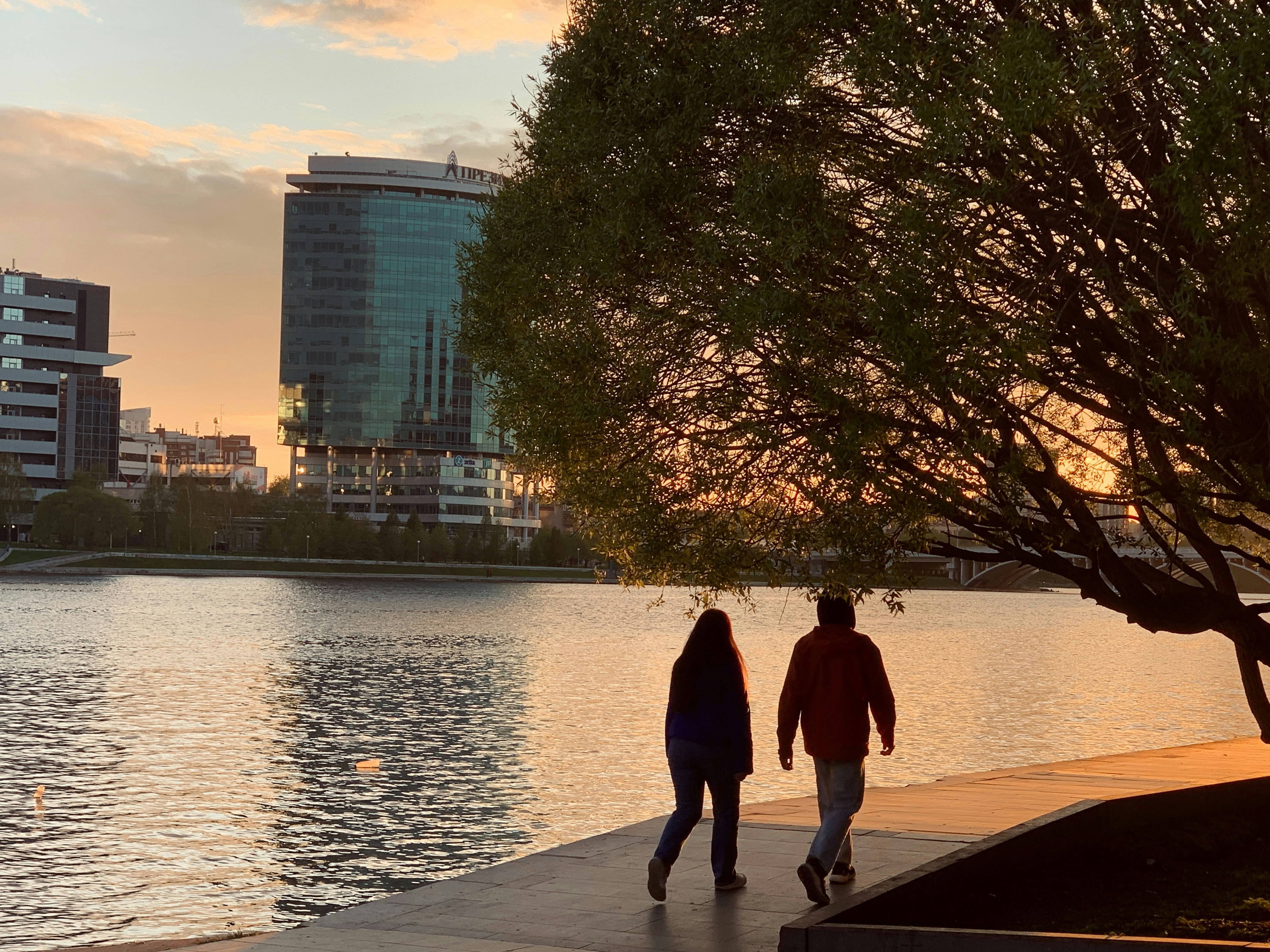 Couple walks alongside the water at sunset.
