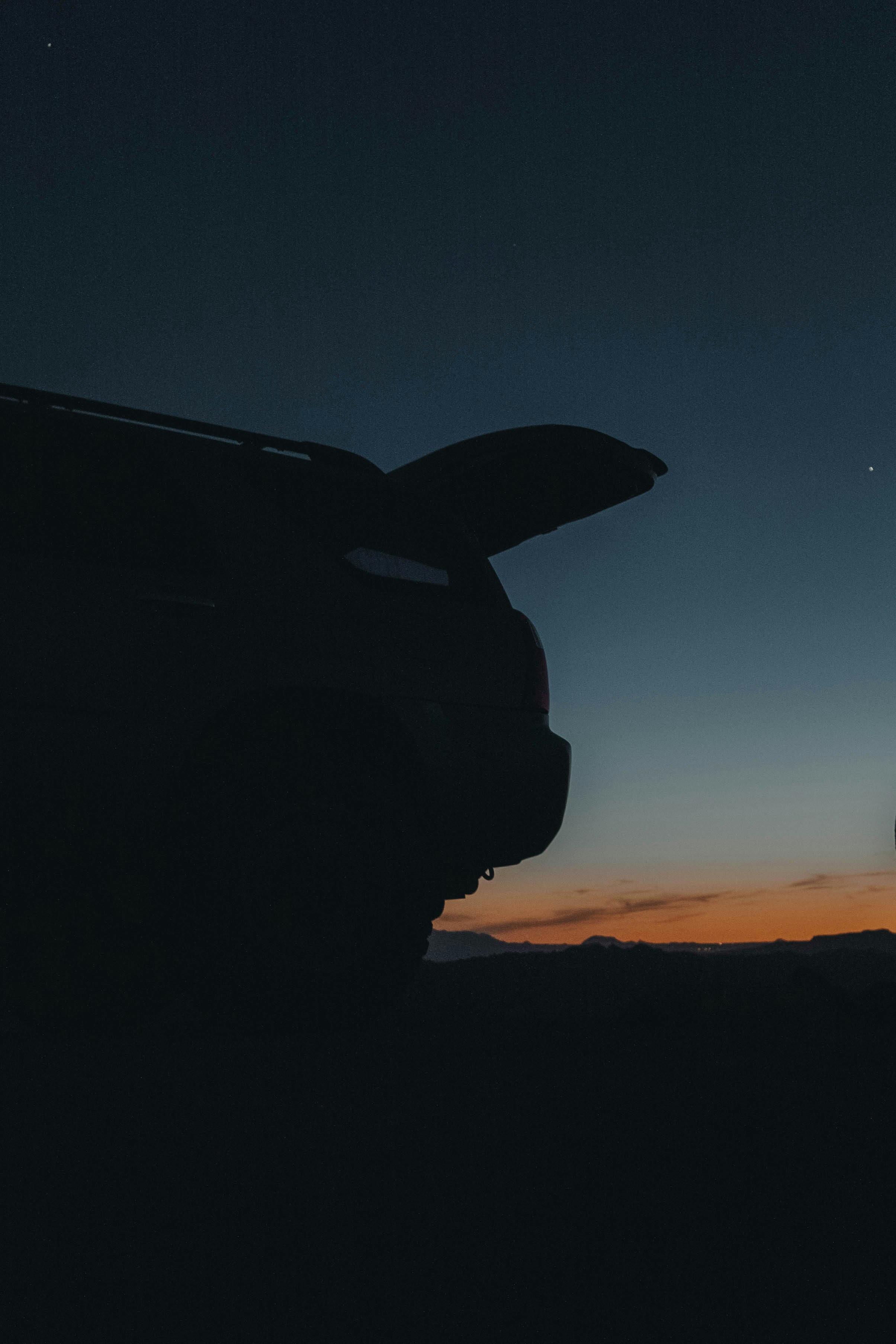 Car silhouette with opened trunk against dusk sky.