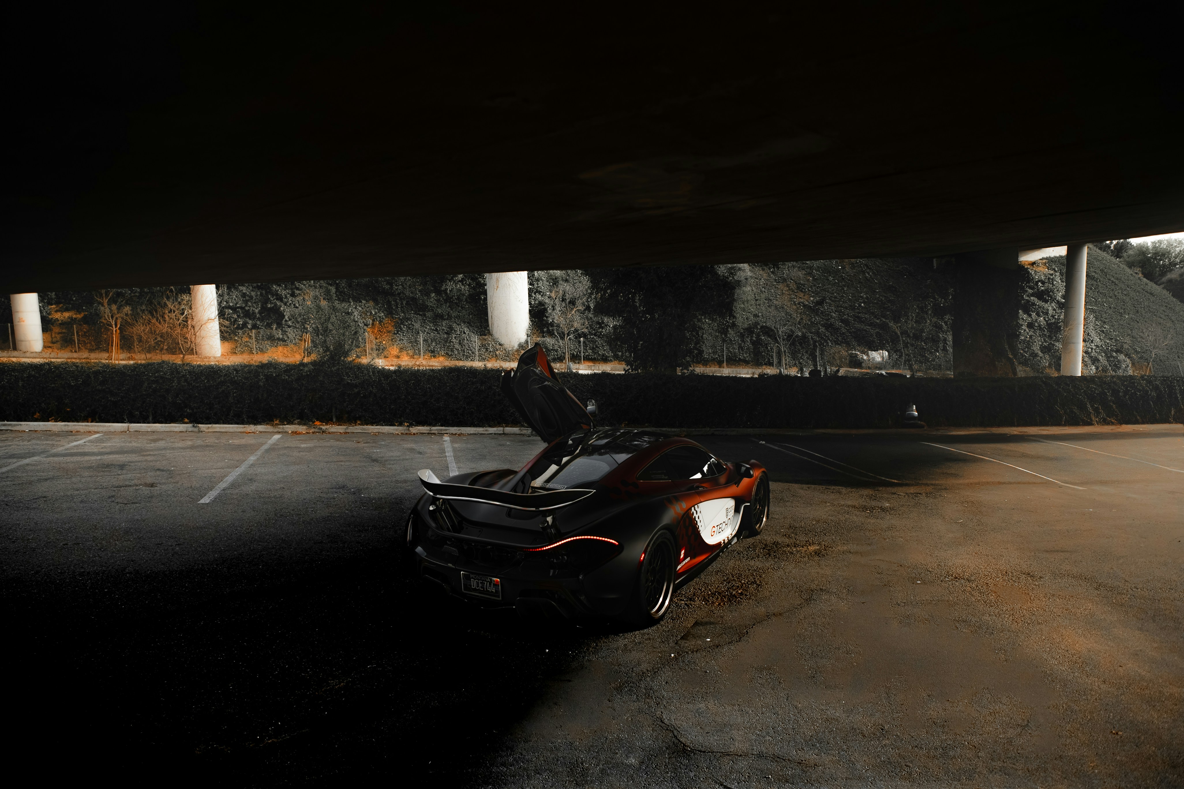 A sleek sports car parked under a dark bridge.