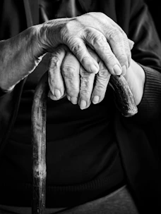 An elderly person's hands rest on a cane.