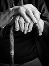 An elderly person's hands rest on a cane.