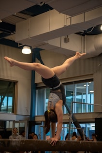 A gymnast balances in a handstand on the beam.