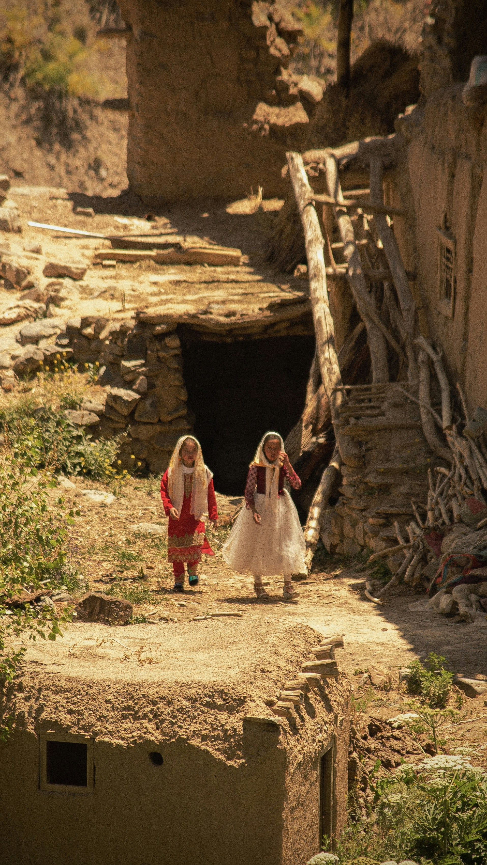Two girls walk through a rustic village.