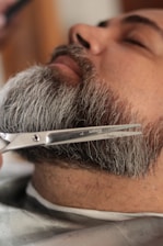 Someone is trimming a man's beard with scissors.