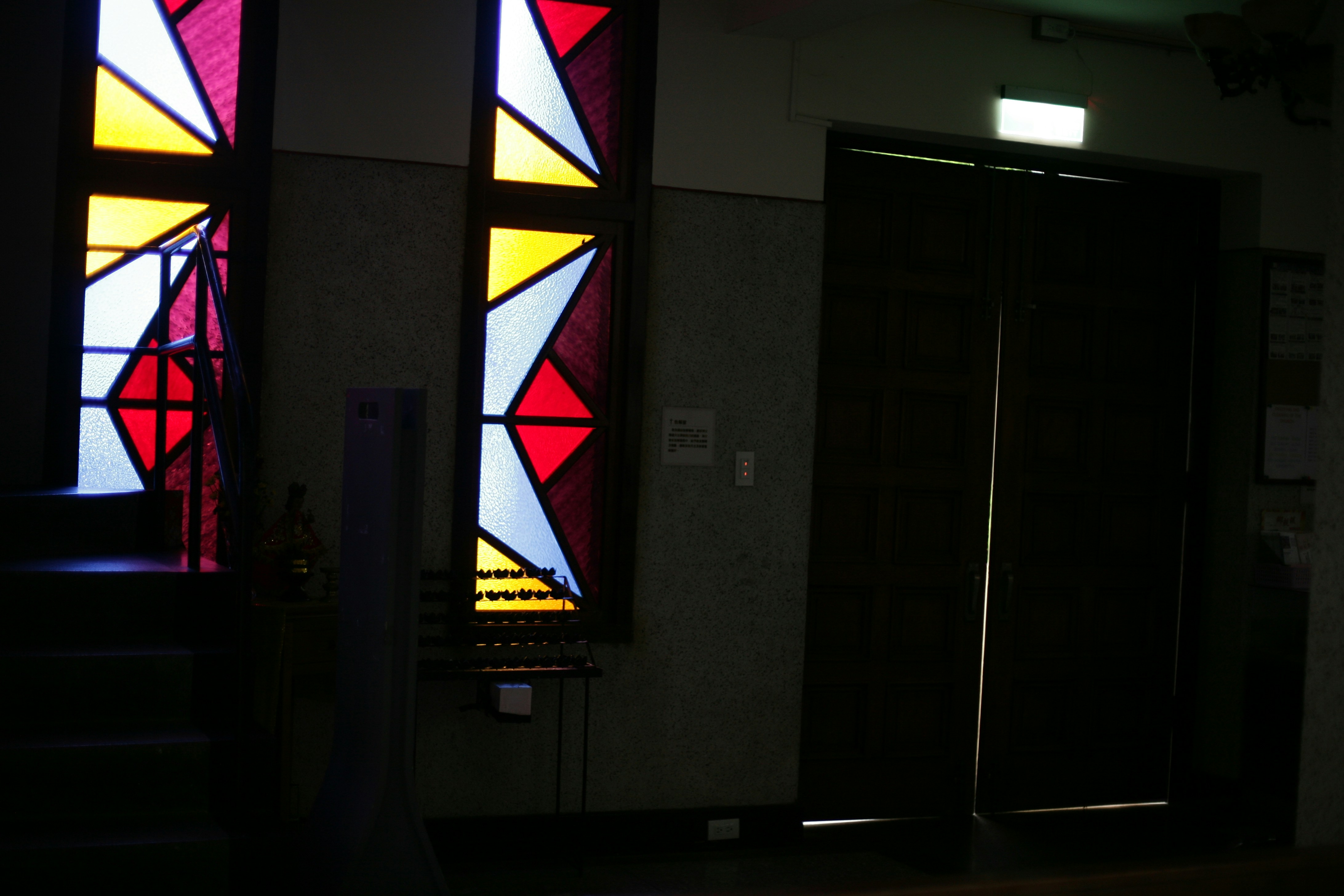 Stained glass windows illuminate a dark hallway.