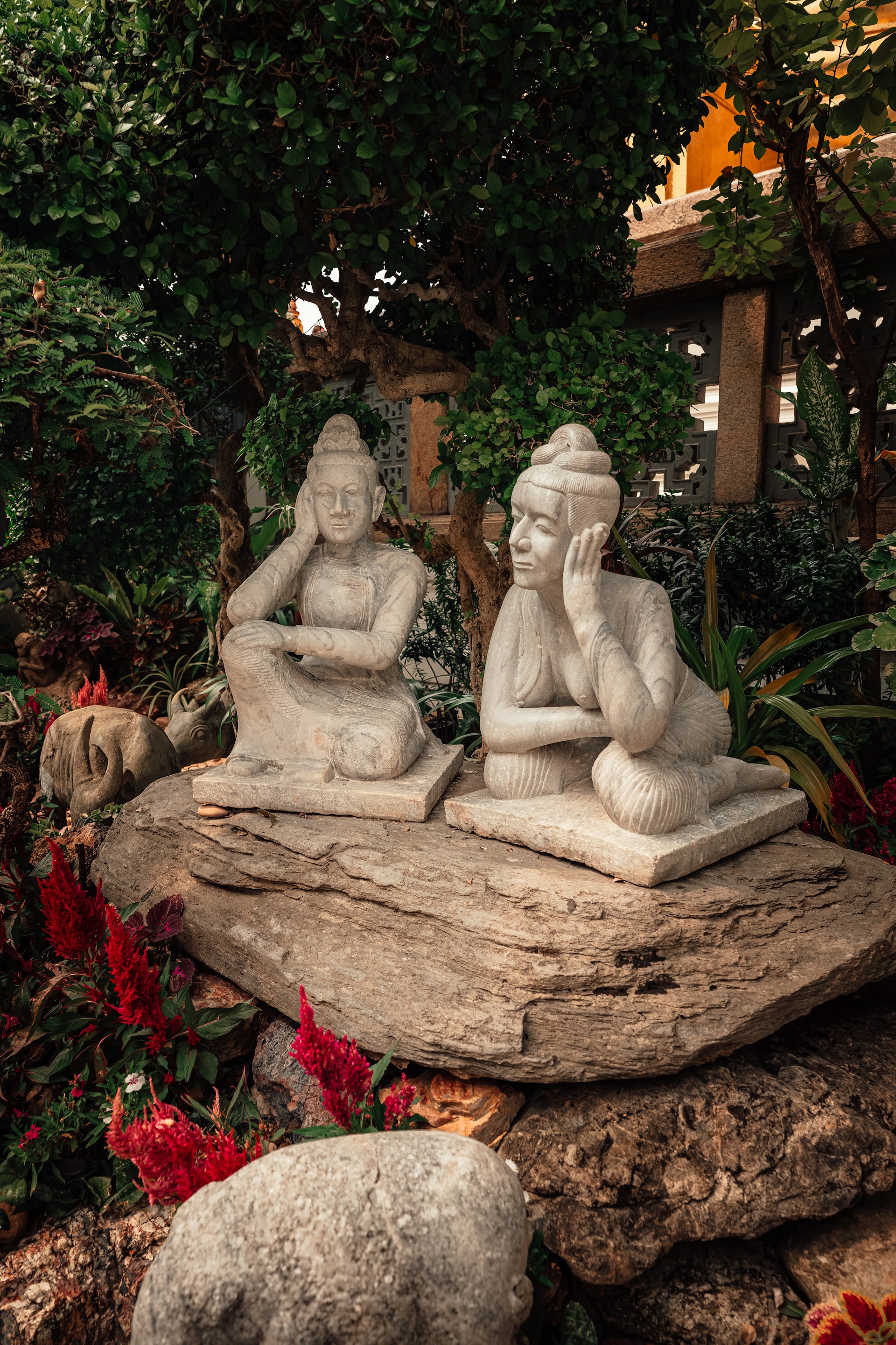 Two serene statues sit in a lush garden.