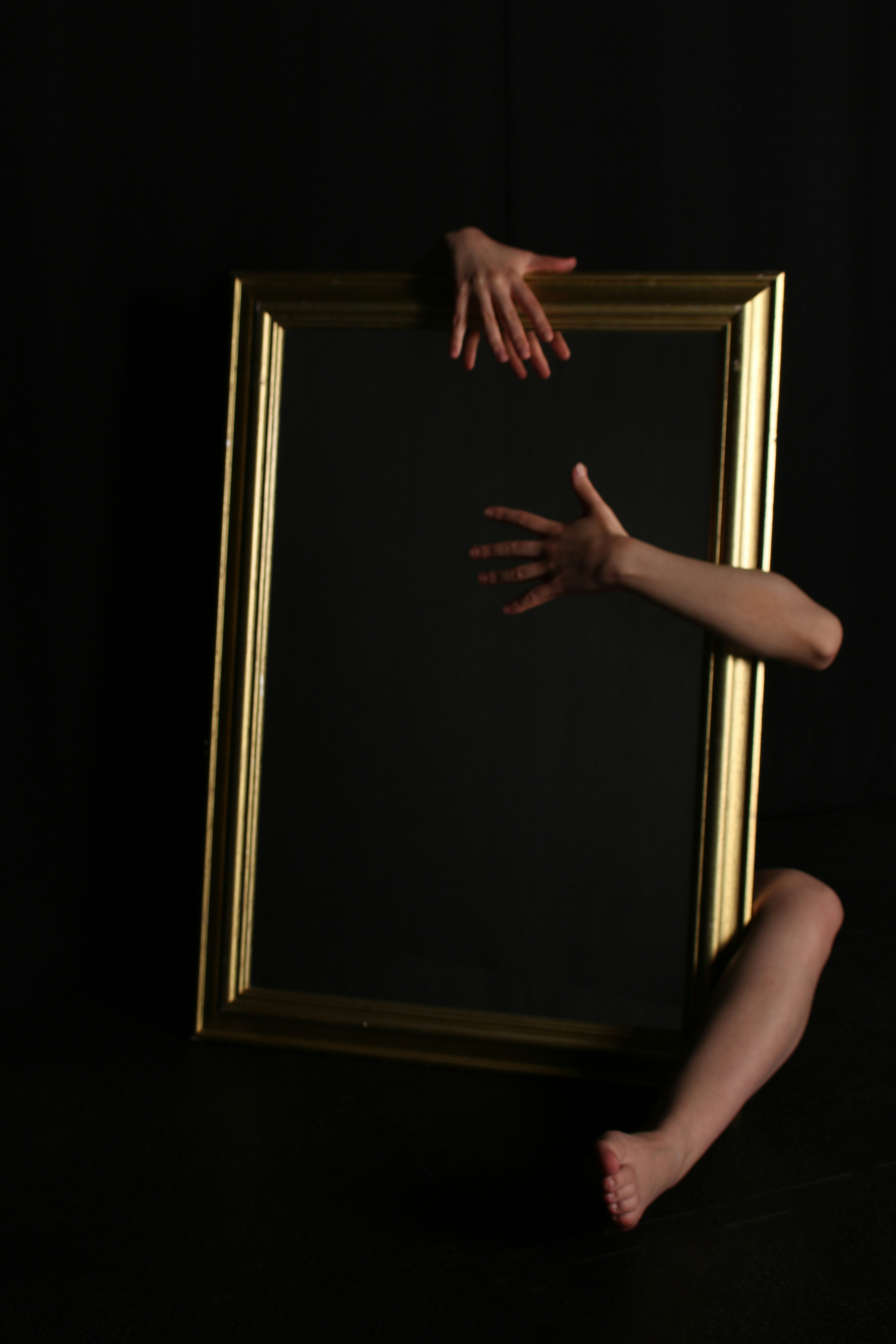 Hands and leg emerge from a framed mirror.