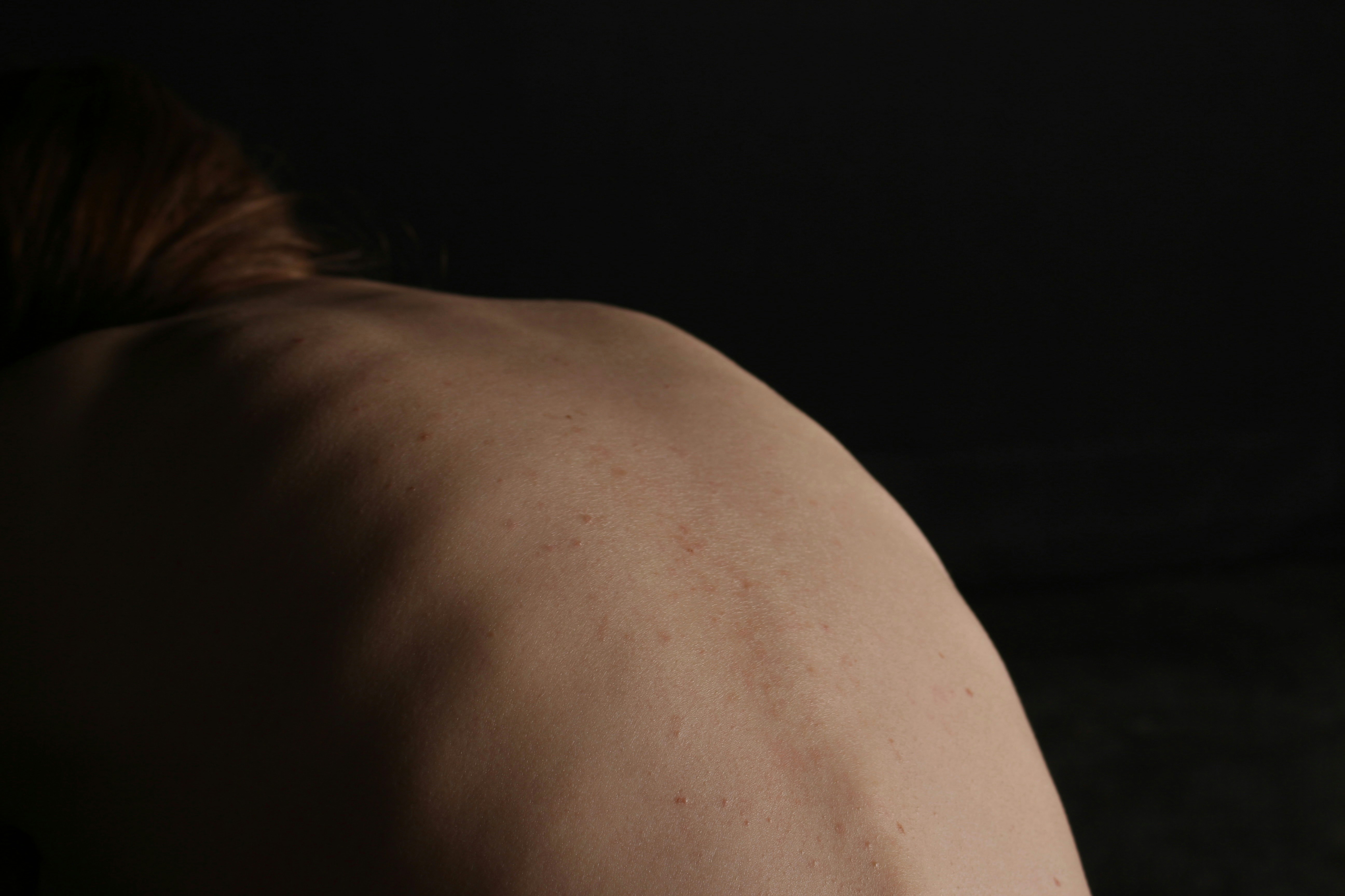 A bare back is illuminated in the darkness.