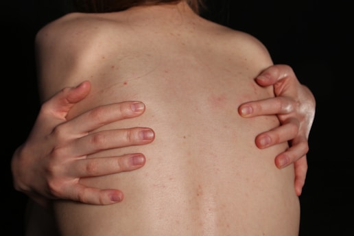 A person embraces their back with both hands.
