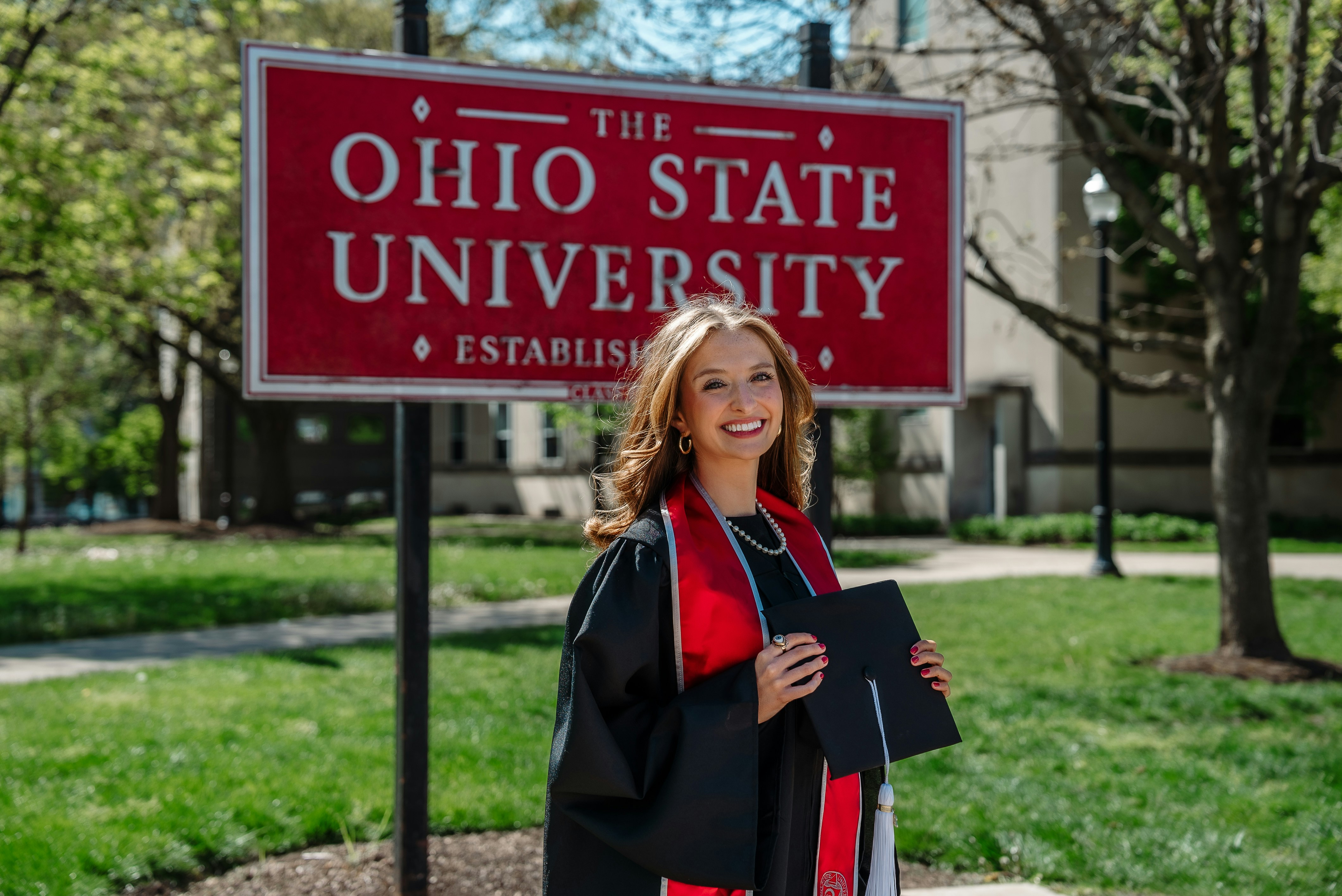 A graduate smiles in front of ohio state university's sign.