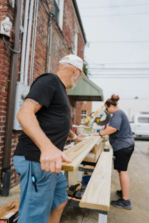 Deux personnes travaillent le bois à l'extérieur.