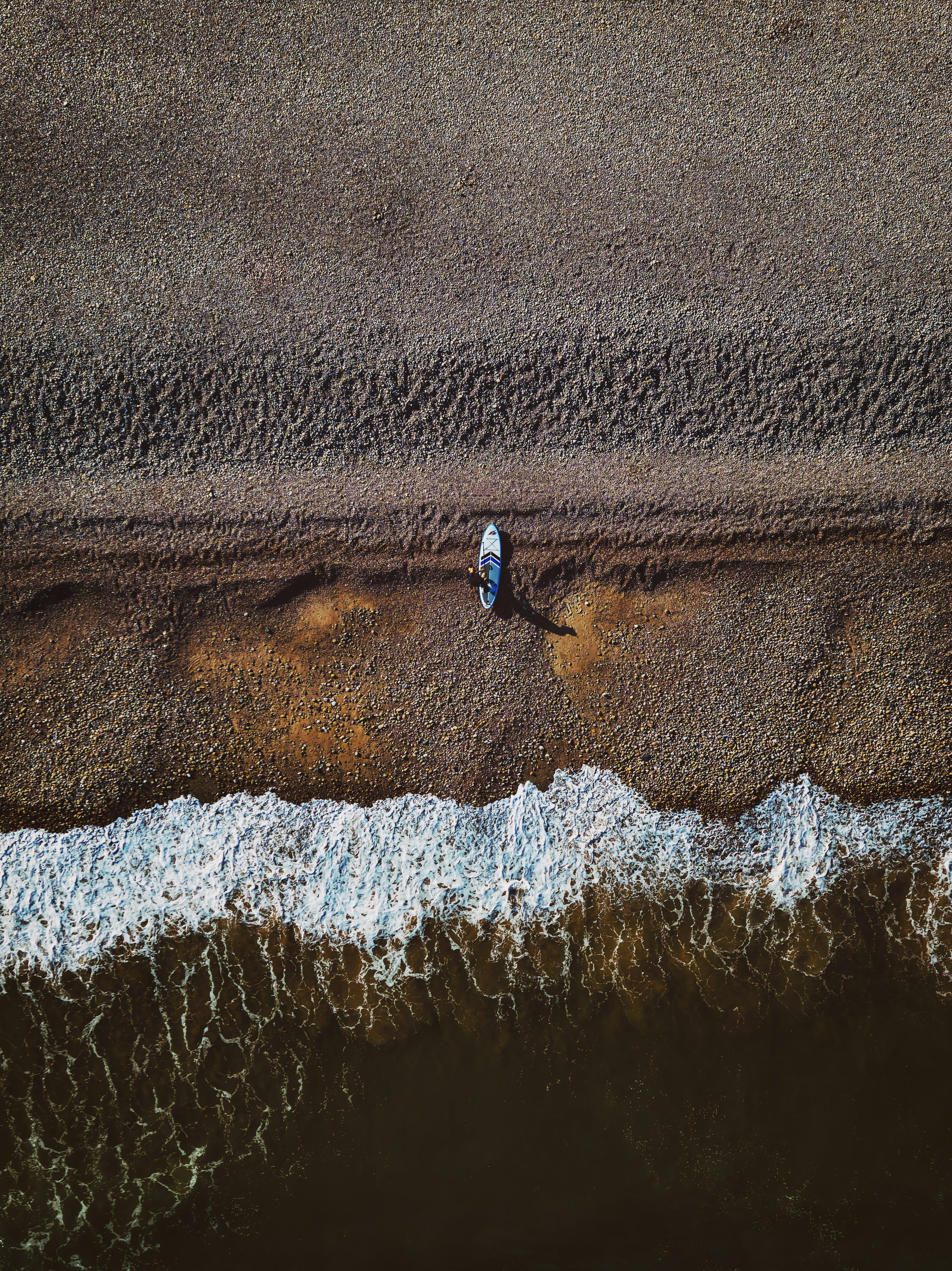 A paddleboard rests on the beach near waves.