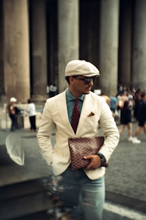 A stylish man poses in front of a columned building.