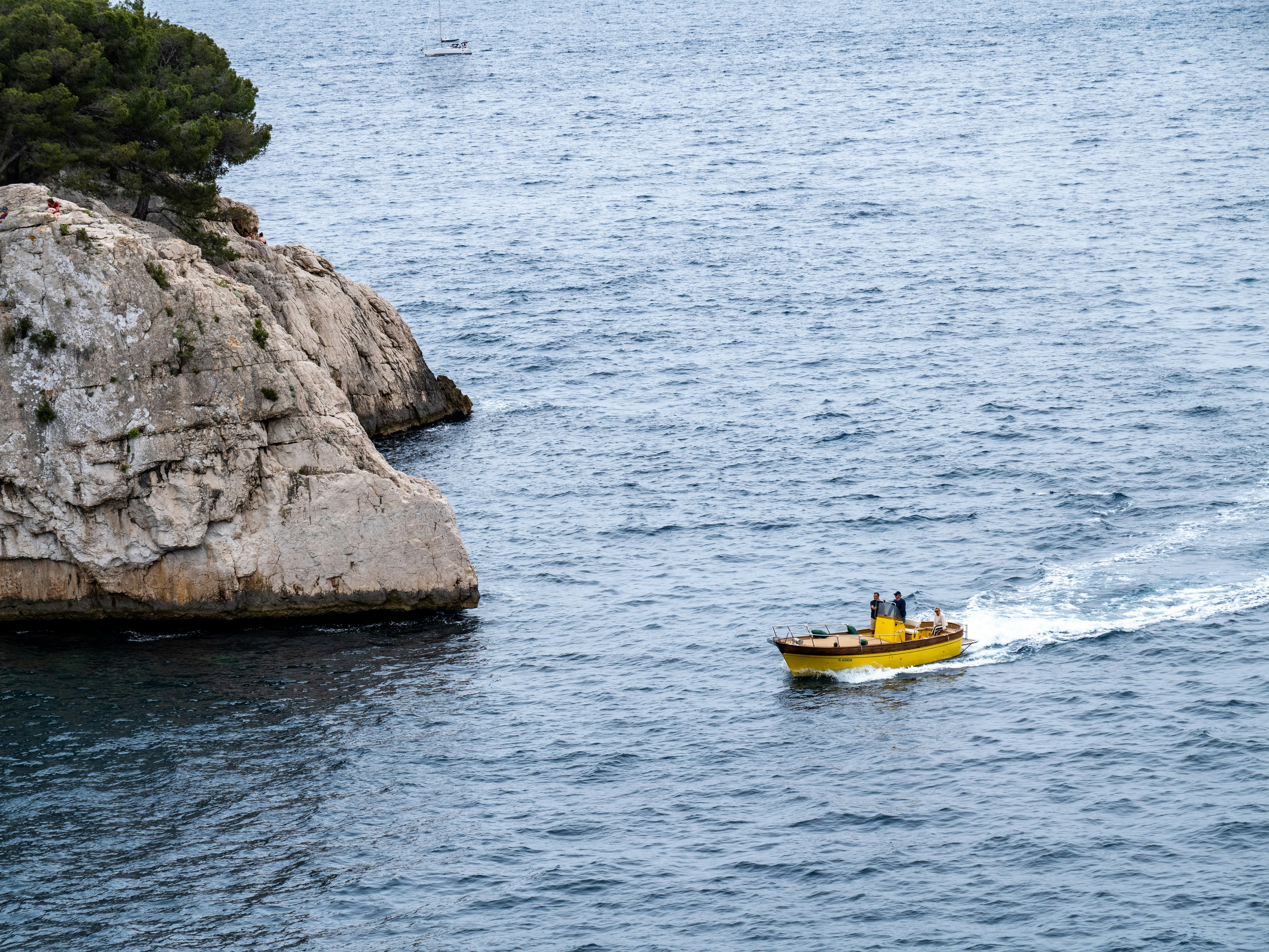 A yellow boat sails near rocky cliffs.