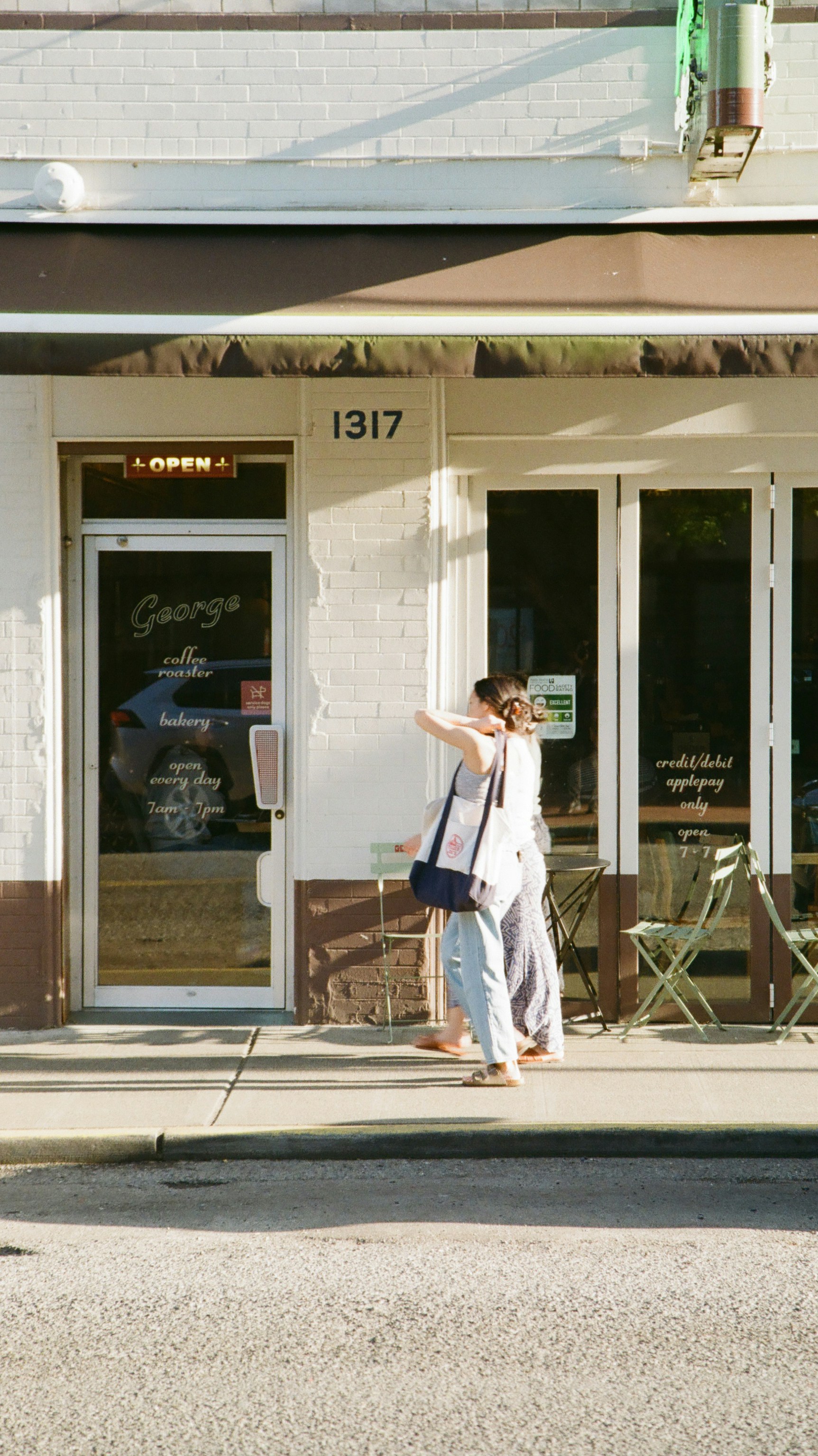 Two women walk past a bakery.