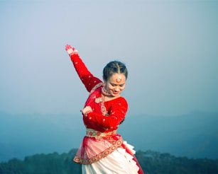A woman performs traditional dance with a mountain view.