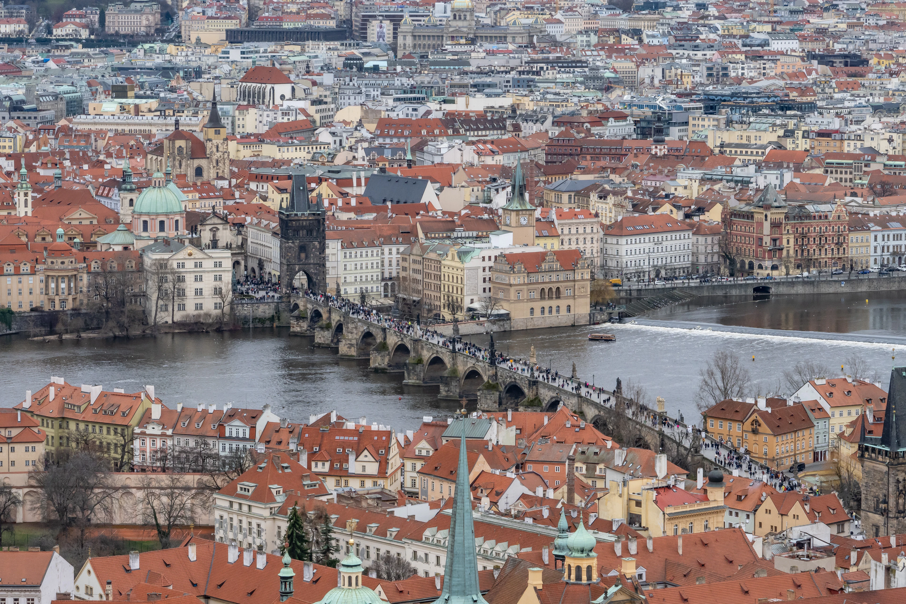Aerial view across Prague's terracotta rooftops to Charles Bridge and its bridge tower crossing the Vltava river