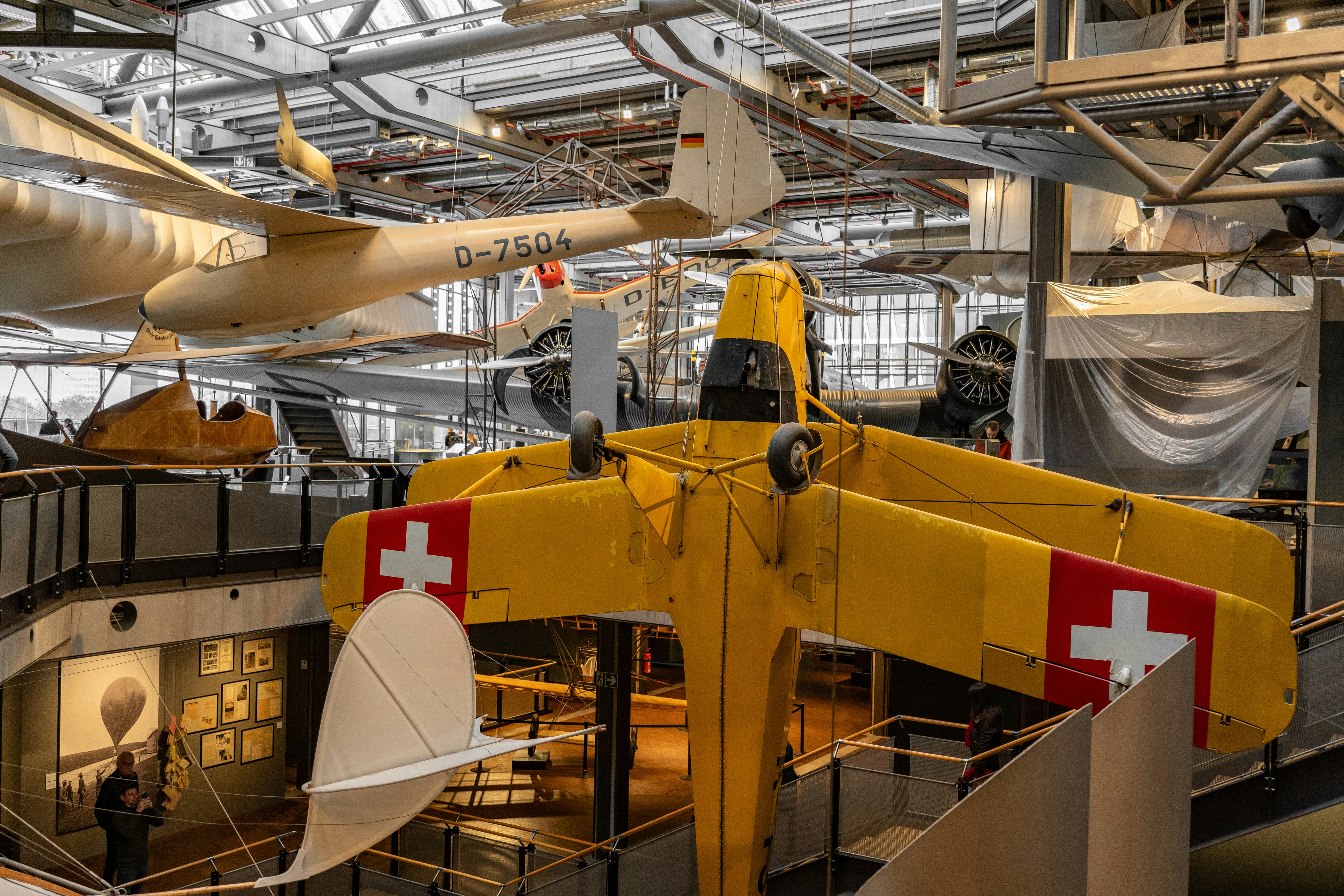 Yellow biplane with swiss crosses hangs in museum.