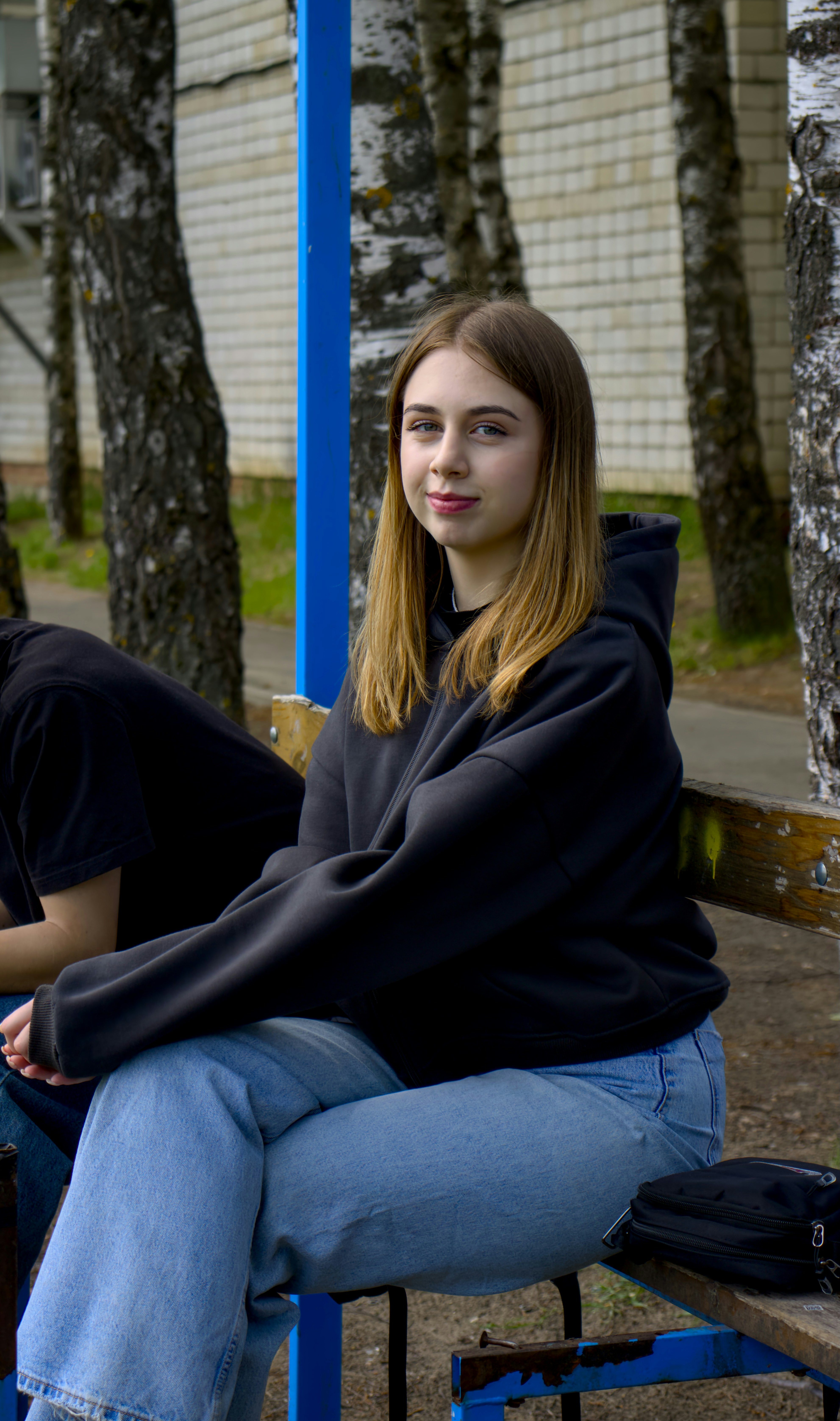 A young woman smiles outdoors, sitting down.