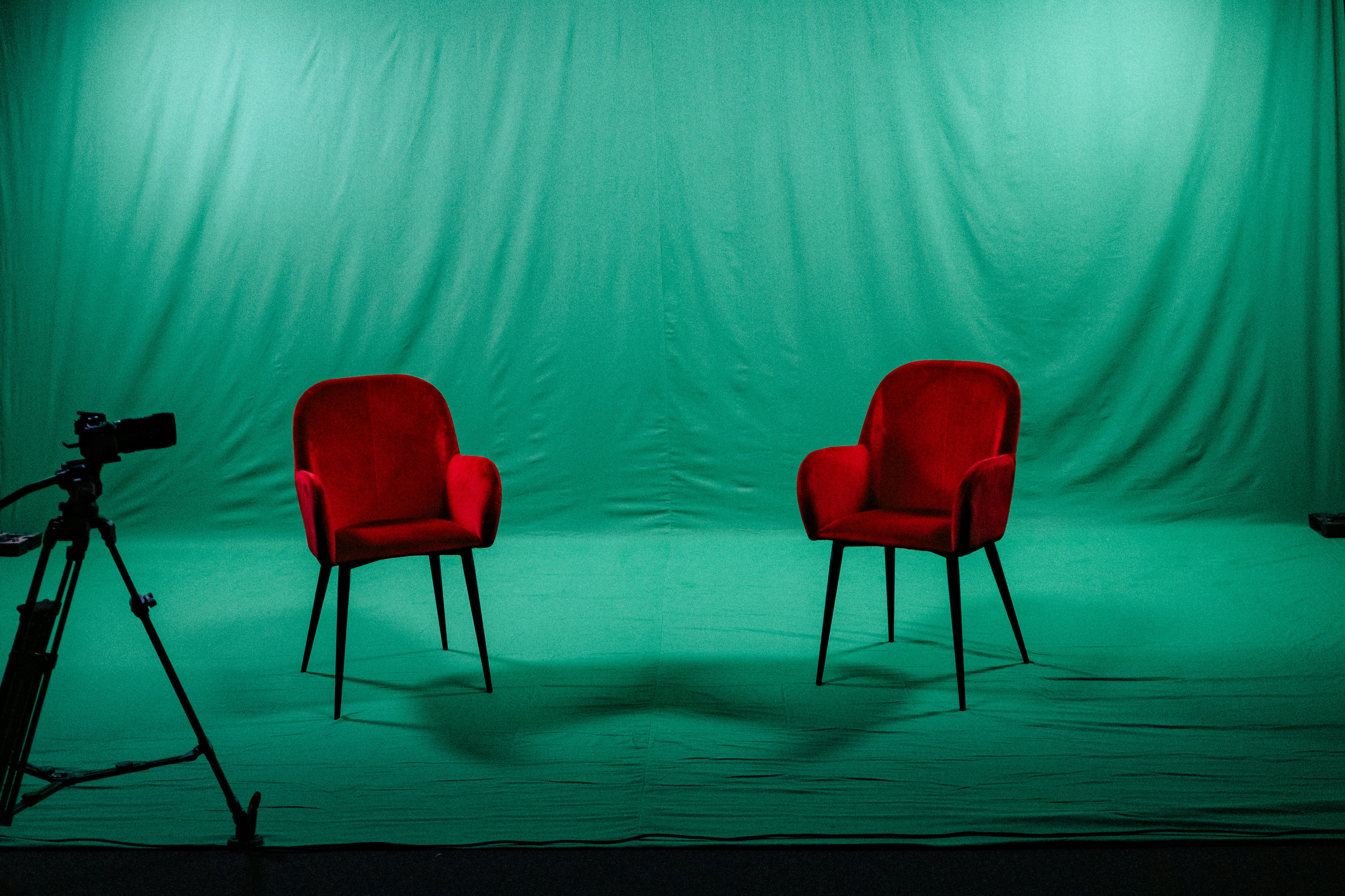 Two red chairs sit before a green screen.