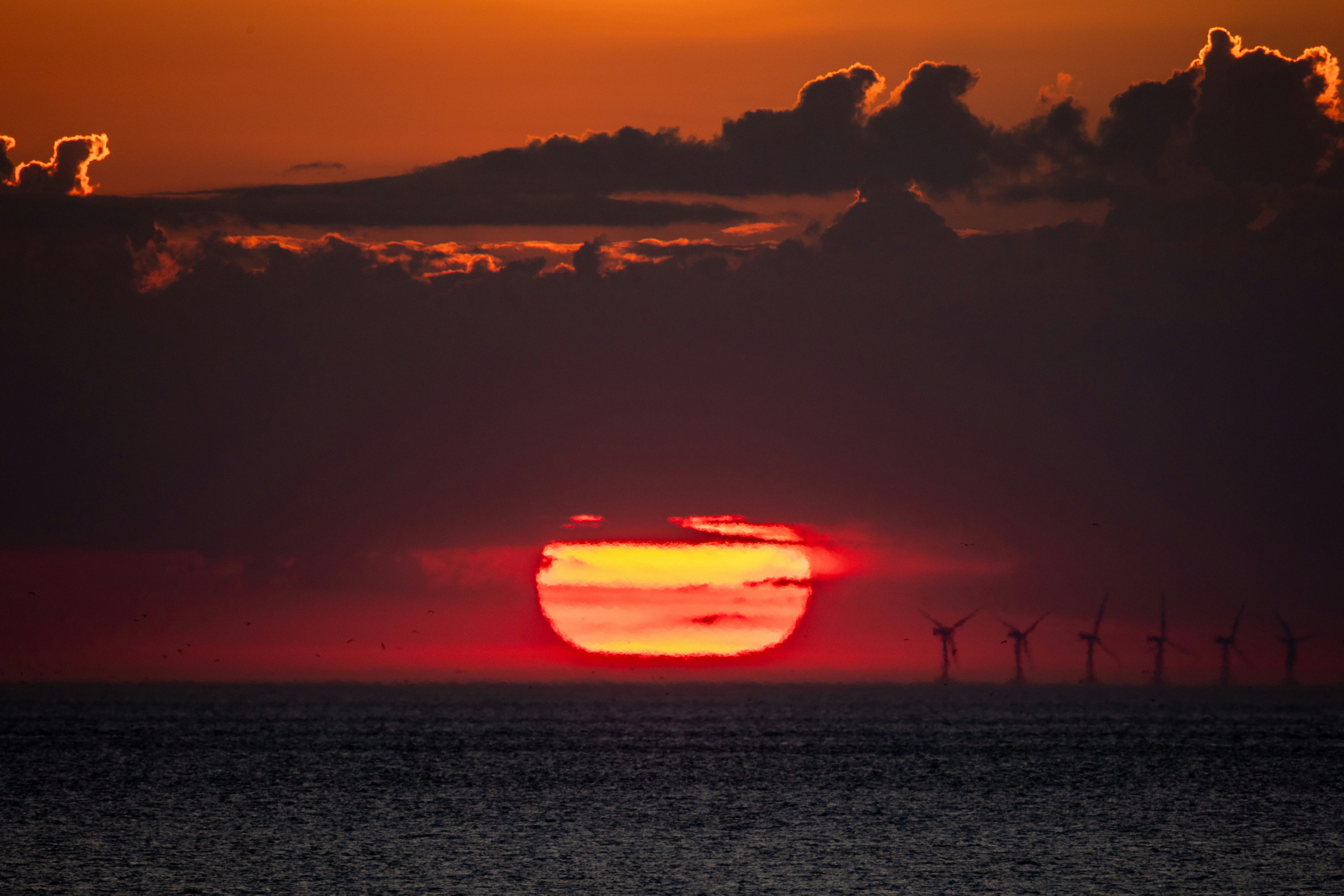 Crimson sunset over the ocean with wind turbines.