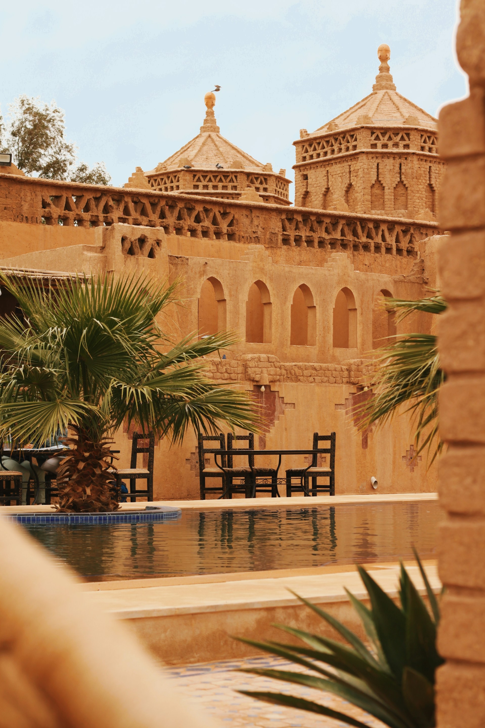 A beautiful moroccan-style building surrounds a pool.