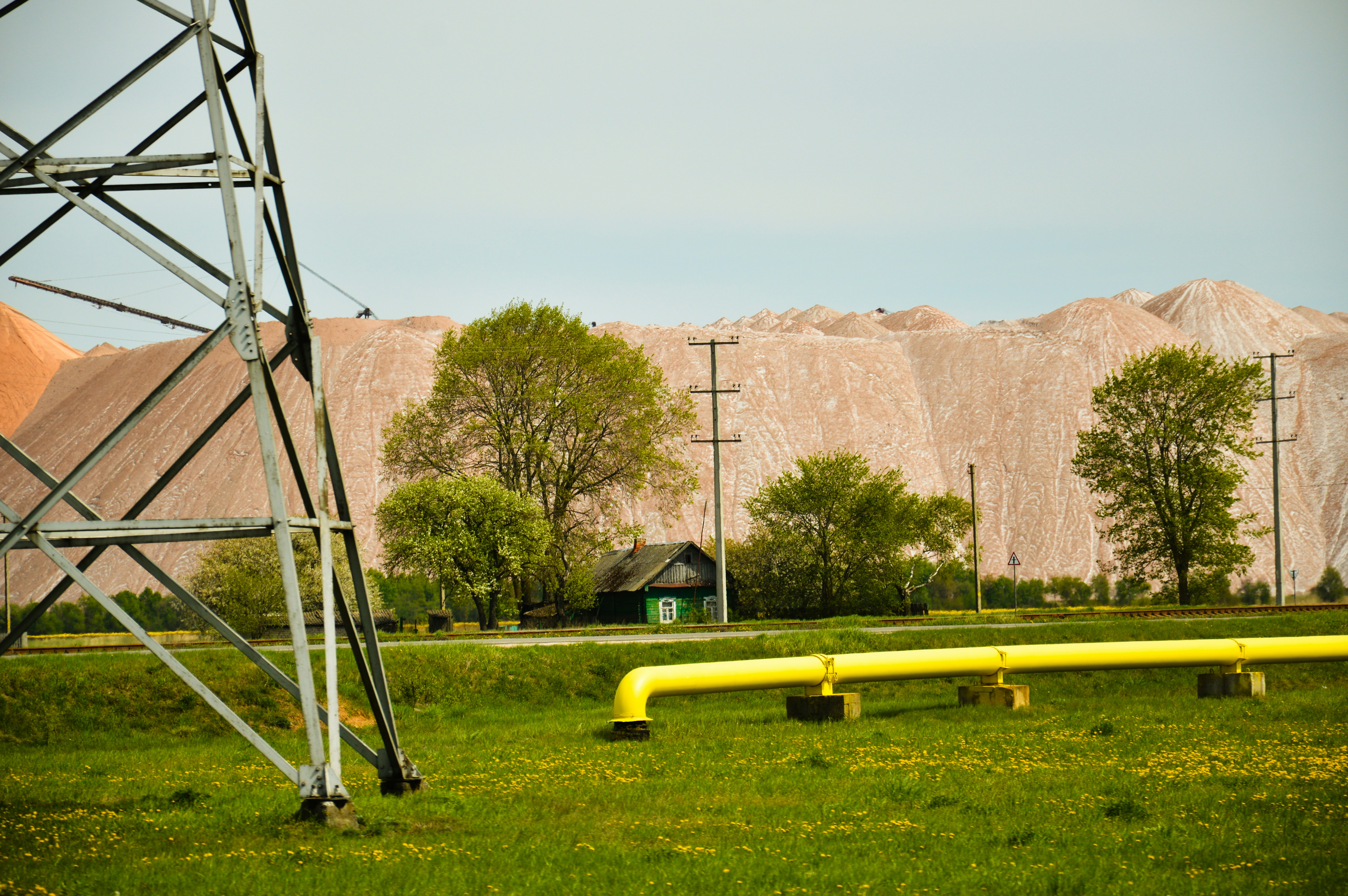 Power line, pipe, and large earth mound in a field. (Photo by Timofey Radkevich on Unsplash)