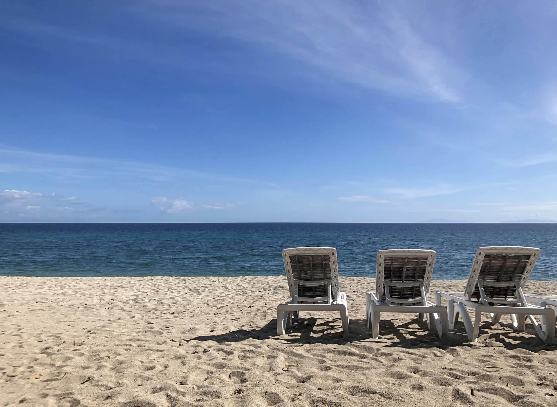 Three empty beach chairs face the ocean.