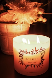 A lit candle with flowers and the word blessed.
