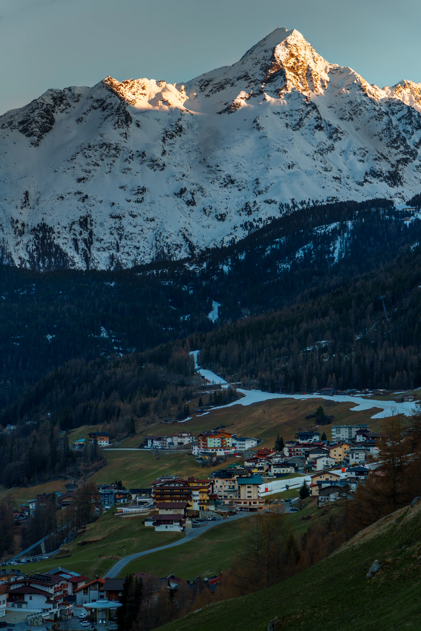 A snow-covered Alpine valley contains buildings and ski slopes.